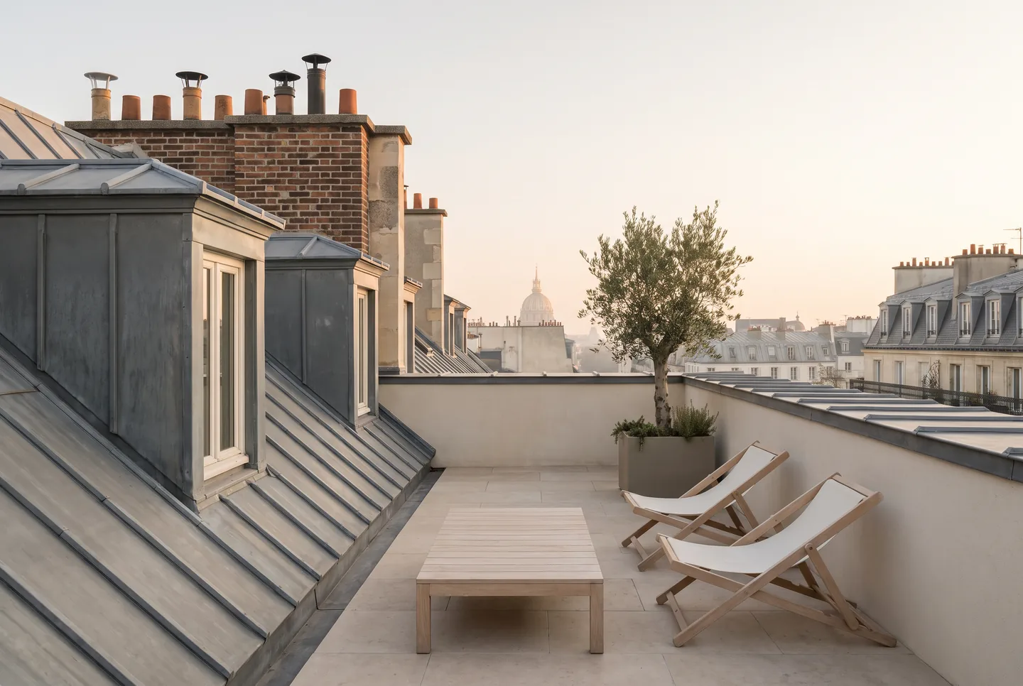 Terrasse aménagée sur les toits de zinc : mobilier bas, olivier en bac, dôme à l’horizon